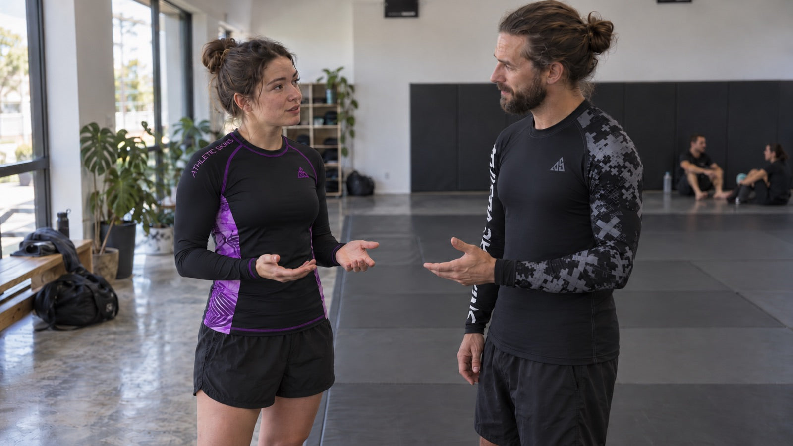 AI-generated photographic scene of a beginner and instructor discussing no-gi class clothing, wearing Athletic Skins Purple/Black and Black/Grey tops.